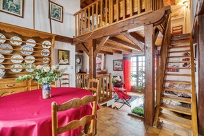 Spiseområde med rødt borddække, træstole, en vase med blomster og en trappe til et loft.