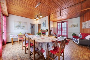 Een eetruimte met een ronde tafel, stoelen en een tafelkleed met een rood-wit patroon.