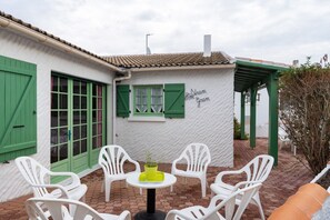 Een terras met witte plastic stoelen en een kleine tafel, een wit gebouw met groene luiken, en een bordje met de tekst 'St. Stram Gram'.