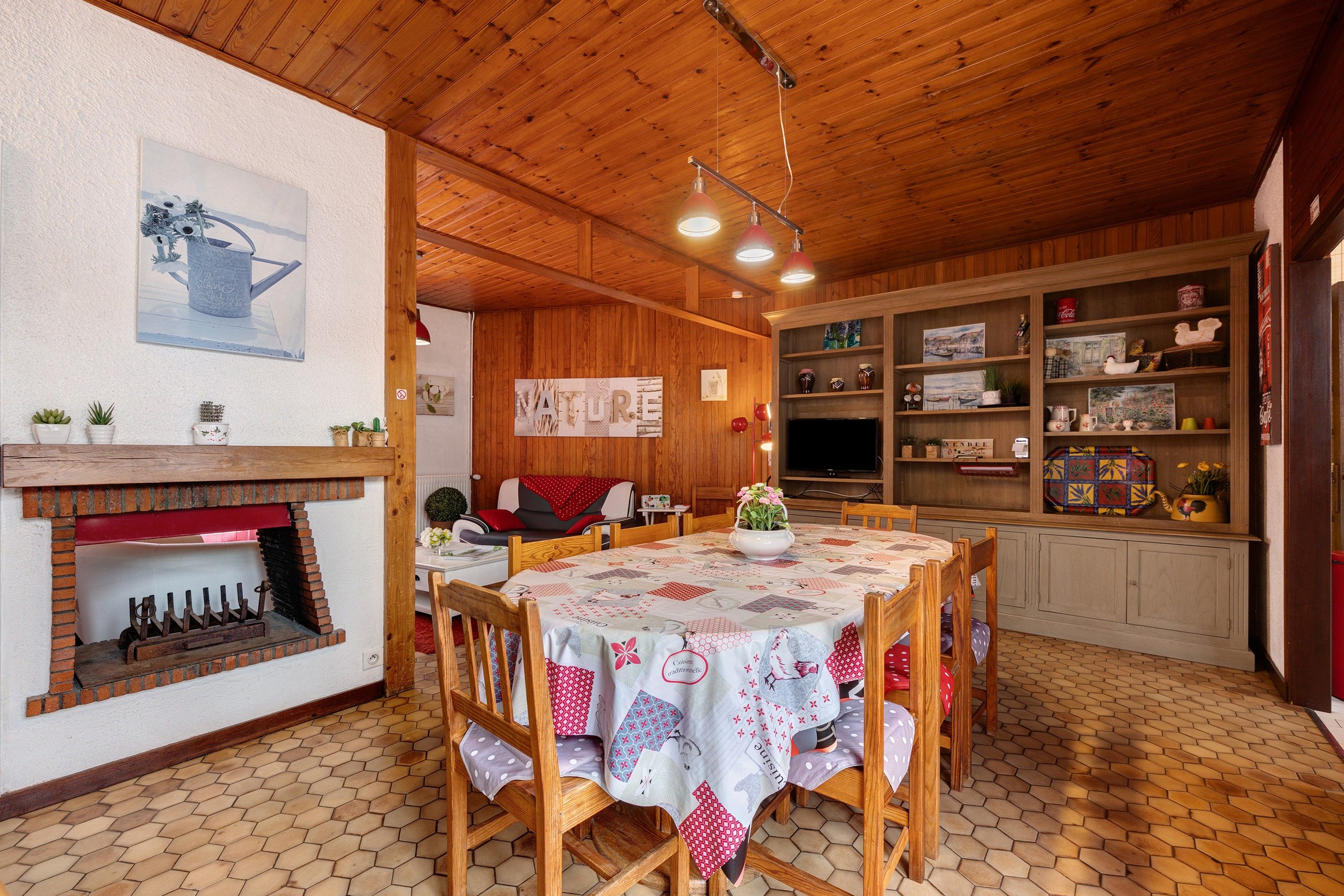 Uma área de refeições acolhedora com mesa de madeira, cadeiras, lareira de tijolos e cozinha com prateleiras.