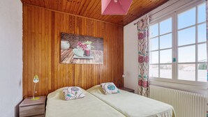 Een kamer met houten paneelwanden, een bed met bloemenbedrukte lakens, een nachtkastje met een lamp en een raam met behang gordijnen.