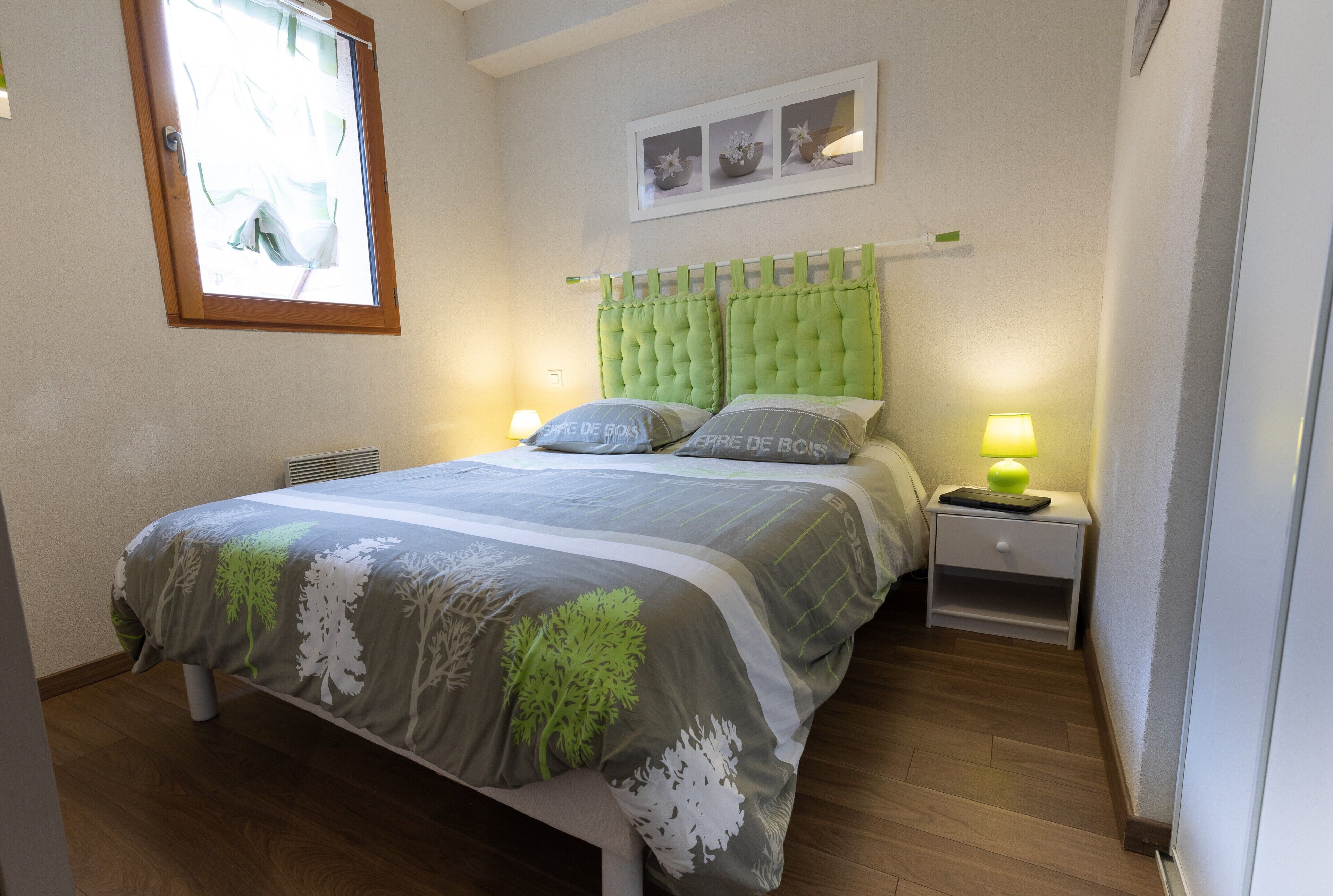 Een slaapkamer met een bed, nachtkastjes, een raam en een wandplank met decoratieve objecten.