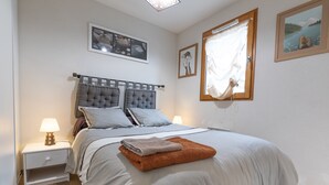 A neatly made bed with a grey headboard, a bedside lamp, and a window with curtains. - Apartment 'Le Bois De Marie' with Mountain View, Private Terrace and Wi-Fi (Barèges)
