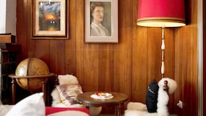 Una habitación con paneles de madera, un globo terráqueo sobre un atril, una mesa redonda con una lámpara y cuadros en la pared.