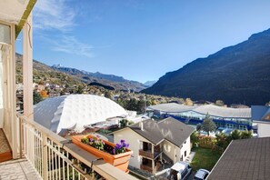 Un immeuble résidentiel doté d’un balcon, d’une structure blanche en forme de dôme et offrant une vue sur une vallée bordée de montagnes.