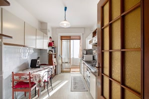 Une cuisine compacte avec des meubles blancs, une table à manger avec des chaises, un four à micro-ondes et une cuisinière.