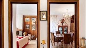 Una habitación con piso de madera, una mesa de comedor con sillas, un candelabro y una estantería.