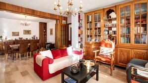 Una sala de estar con un sofá rojo, estanterías de madera, una araña y un comedor.