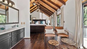 Een modern interieur met een houten plafond, een groot bed, een keukenhoek en een zithoek met twee krukken.