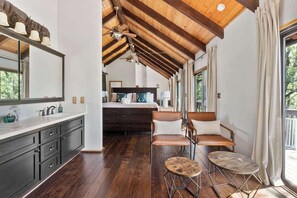 A modern interior with a wooden ceiling, a large bed, a kitchen area, and a seating area with two stools.