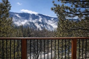 Paesaggio montano con cielo sereno, una strada e una ringhiera di legno in primo piano.