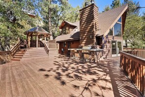 Un pontile in legno con un gazebo, un camino in pietra e un'ampia finestra con vista su una zona boscosa.