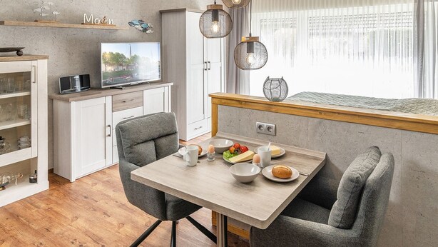 Una cocina compacta con zona de comedor, televisor y ventana con cortinas.