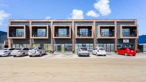 A modern building with a flat roof, multiple balconies, and a parking lot with several cars. - Bushiri's Long Life Building-2BD/1BA APT-Sleeps 4 (Oranjestad)