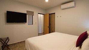 Une chambre à coucher comprenant un lit, un téléviseur fixé au mur, une porte et un appareil de climatisation.