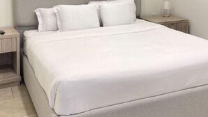 A neatly made bed with a grey headboard and white bedding in a simple, clean room. - Bushiri's Long Life Building-2BD/1BA APT-Sleeps 4 (Oranjestad)