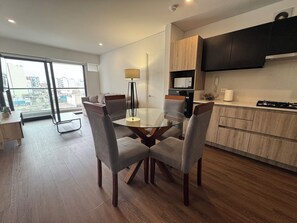 Una cocina moderna con armarios de madera, una estufa empotrada y un comedor con mesa y sillas de vidrio.
