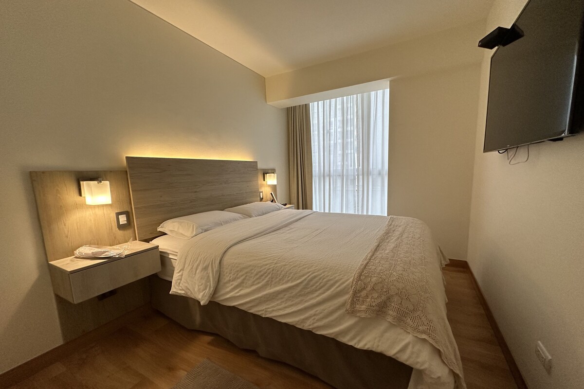 Une chambre d’hôtel avec un lit, des tables de chevet, une télévision et une fenêtre avec des rideaux.