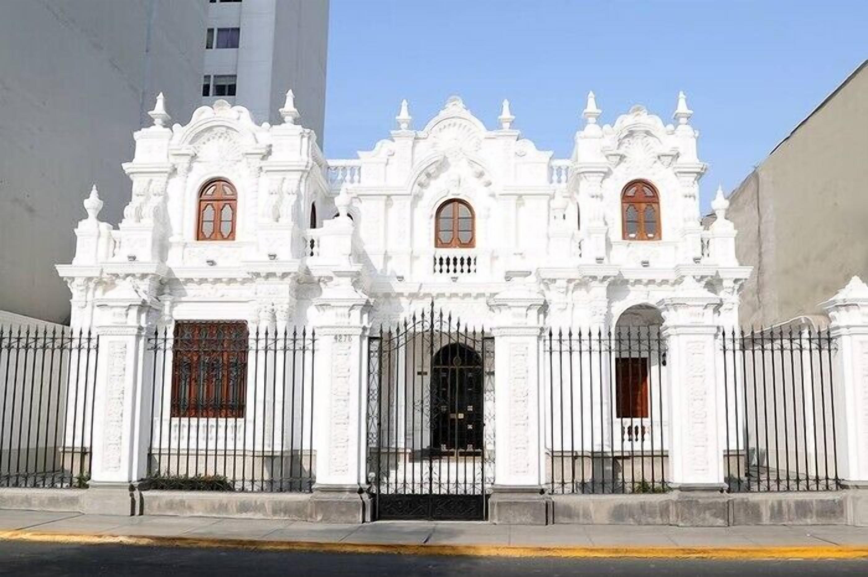 A white colonial-style building with ornate architectural details, a black gate, and a clear sky.