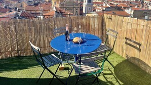 Eine Dachterrasse mit blauem Tisch, zwei Stühlen, einer Champagnerflasche und einem Brotkorb.