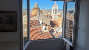 Blick aus einem Fenster auf eine Stadtlandschaft mit Ziegeldächern und historischen Gebäuden.