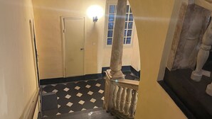 Eine Treppe mit schwarz-weiß kariertem Boden, eine weiße Tür am oberen Ende und eine Leuchte darüber.