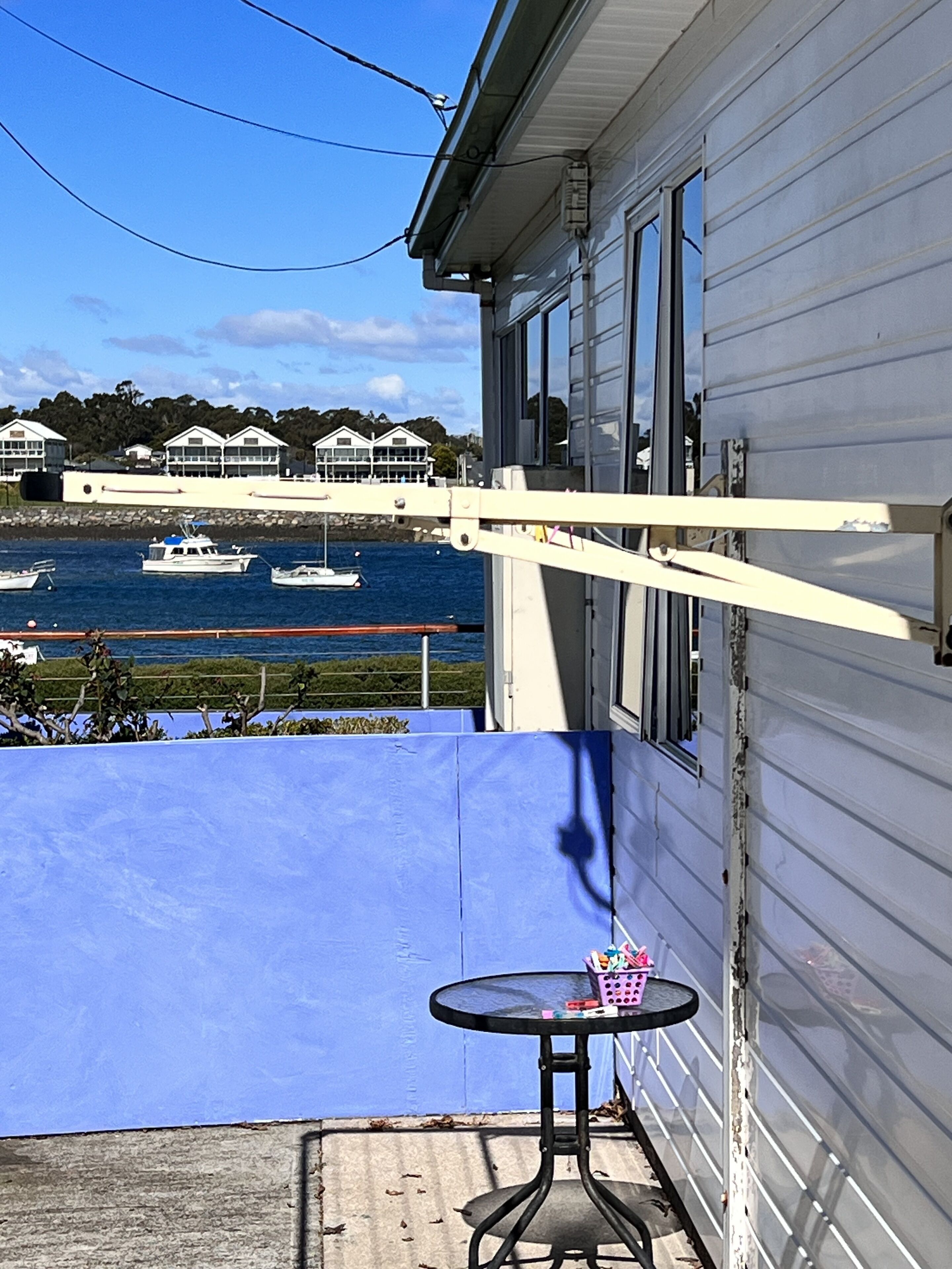 Un balcon donnant sur un port, une petite table ronde et une rambarde bleue.