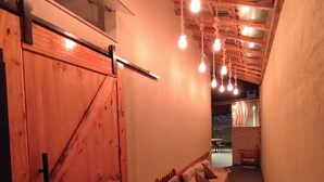 A narrow hallway with a wooden barn door, a bench, and hanging light bulbs.