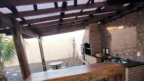 An outdoor bar area with a wooden bar, stools, and a brick oven.
