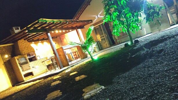 A building with a brick exterior, a covered patio area with seating, and a small garden with a tree.