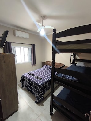 Une chambre avec un lit superposé, un bureau, une chaise, une armoire et un ventilateur de plafond.