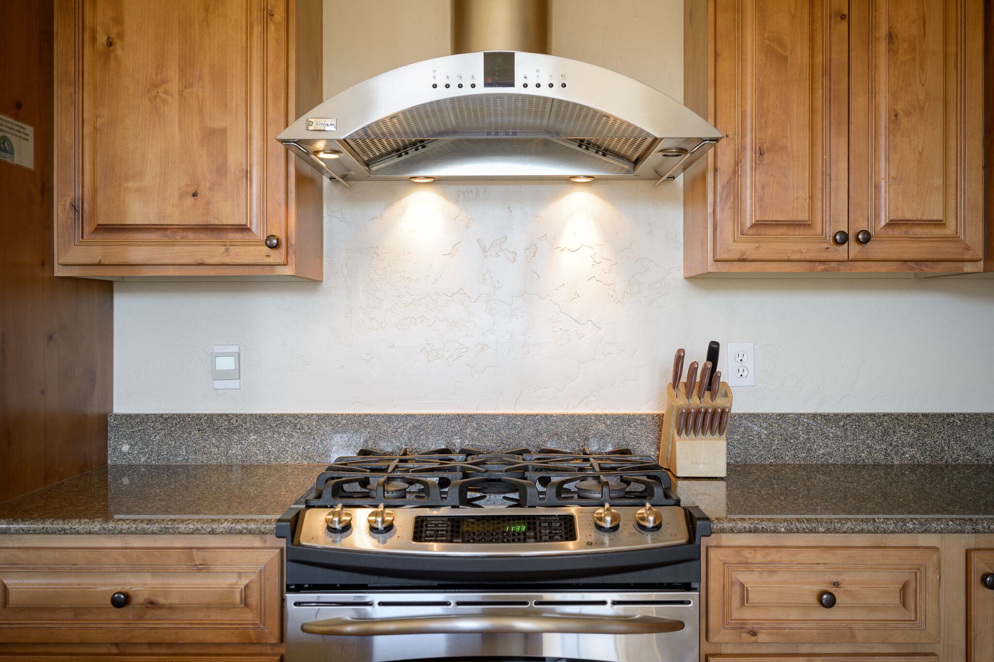Une cuisine avec des meubles en bois, une cuisinière en acier inoxydable et des plans de travail en granit.