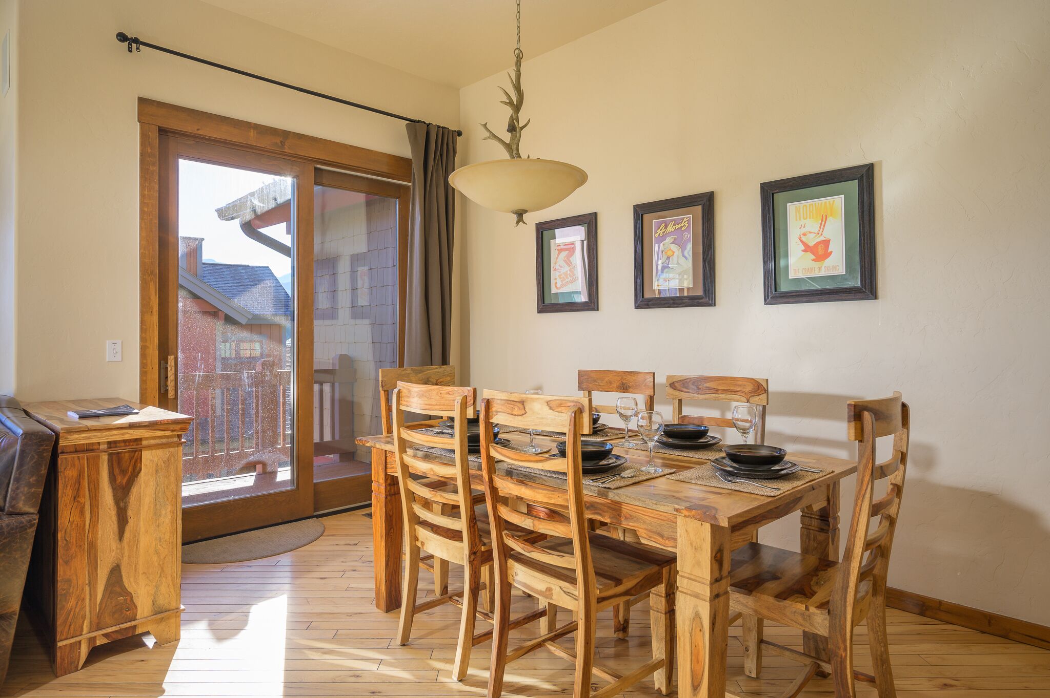 Ein Essbereich mit Holztisch und -stühlen, einer hängenden Leuchte und gerahmten Bildern an der Wand.