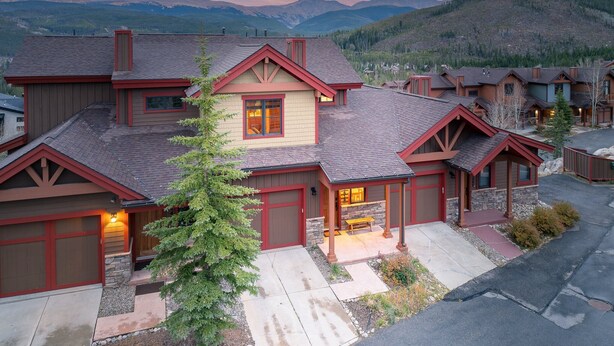 A two-story house with a stone fireplace, a red garage door, and a view of mountains in the background.