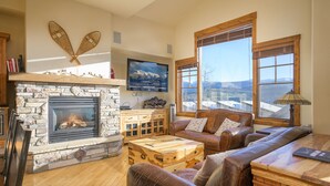 A cozy living room with a stone fireplace, leather furniture, and large windows offering a view of the mountains.