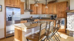 A kitchen with wooden cabinets, a stainless steel refrigerator, a granite countertop, and a stone fireplace.