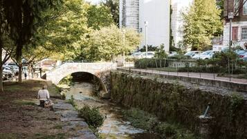 Un pont de pierre enjambe un petit ruisseau dans un parc, avec des arbres et un bâtiment en arrière-plan.