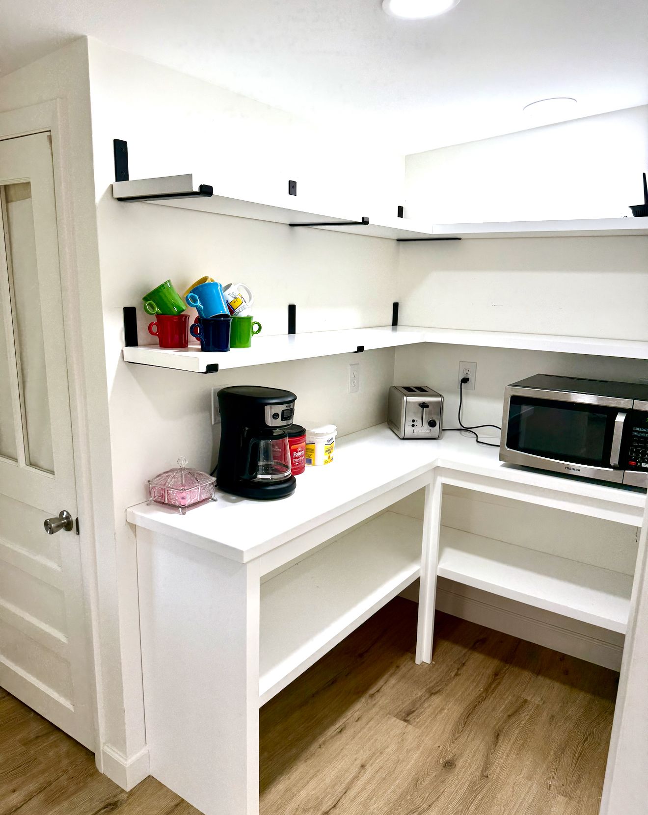 Une petite cuisine équipée avec des meubles blancs, une machine à café, un grille-pain et un four à micro-ondes.