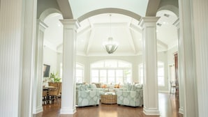 A spacious living room with a high ceiling, large windows, and a central seating area with patterned sofas.