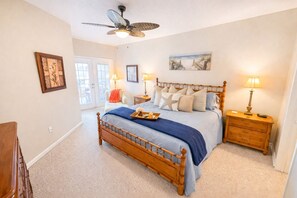 A bedroom with a wooden bed, a ceiling fan, and a beach-themed painting. - Relaxed Resort-Style Coastal Villa/Pools/Hot tubs/Gym/2 Min to Beach. Gated! (Gulfport)