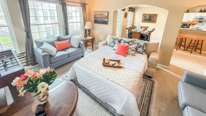 A bedroom with a large bed, a sofa, a dining area, and a view of the outside.