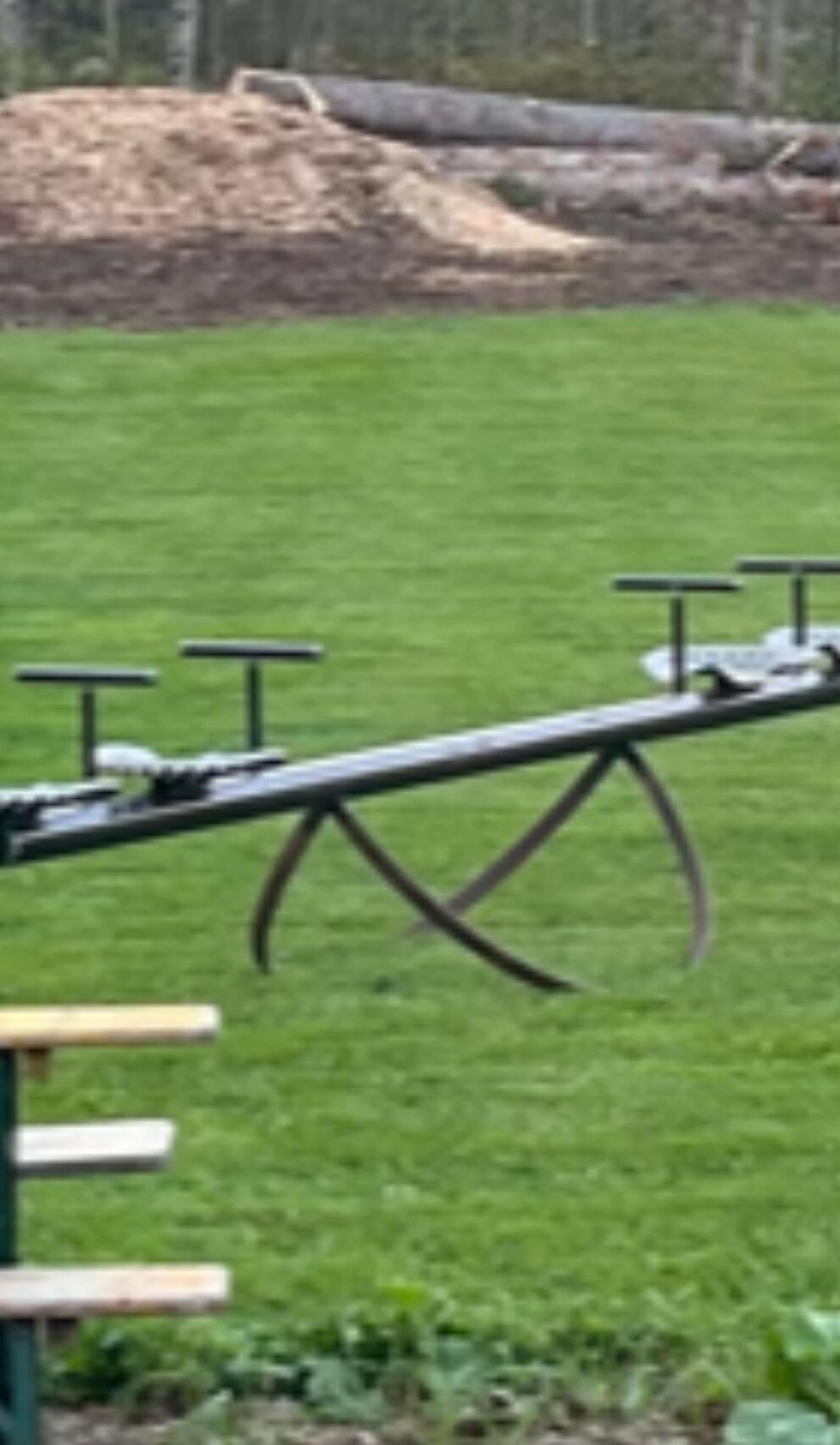 A seesaw with a green metal frame and a wooden seat in a grassy area.