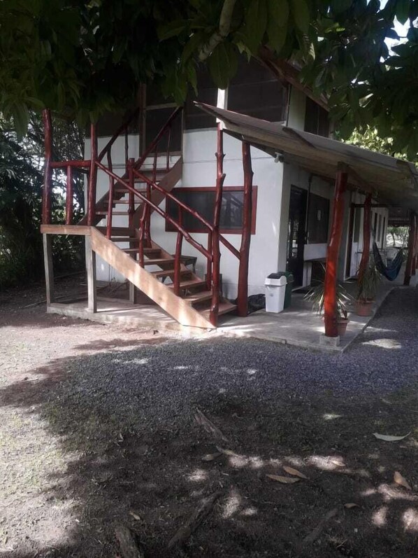Un edificio con una escalera de madera que lleva a un espacio cubierto con una hamaca.