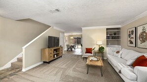 Ein Wohnzimmer mit Sofa, Couchtisch, Fernseher und einer Treppe.