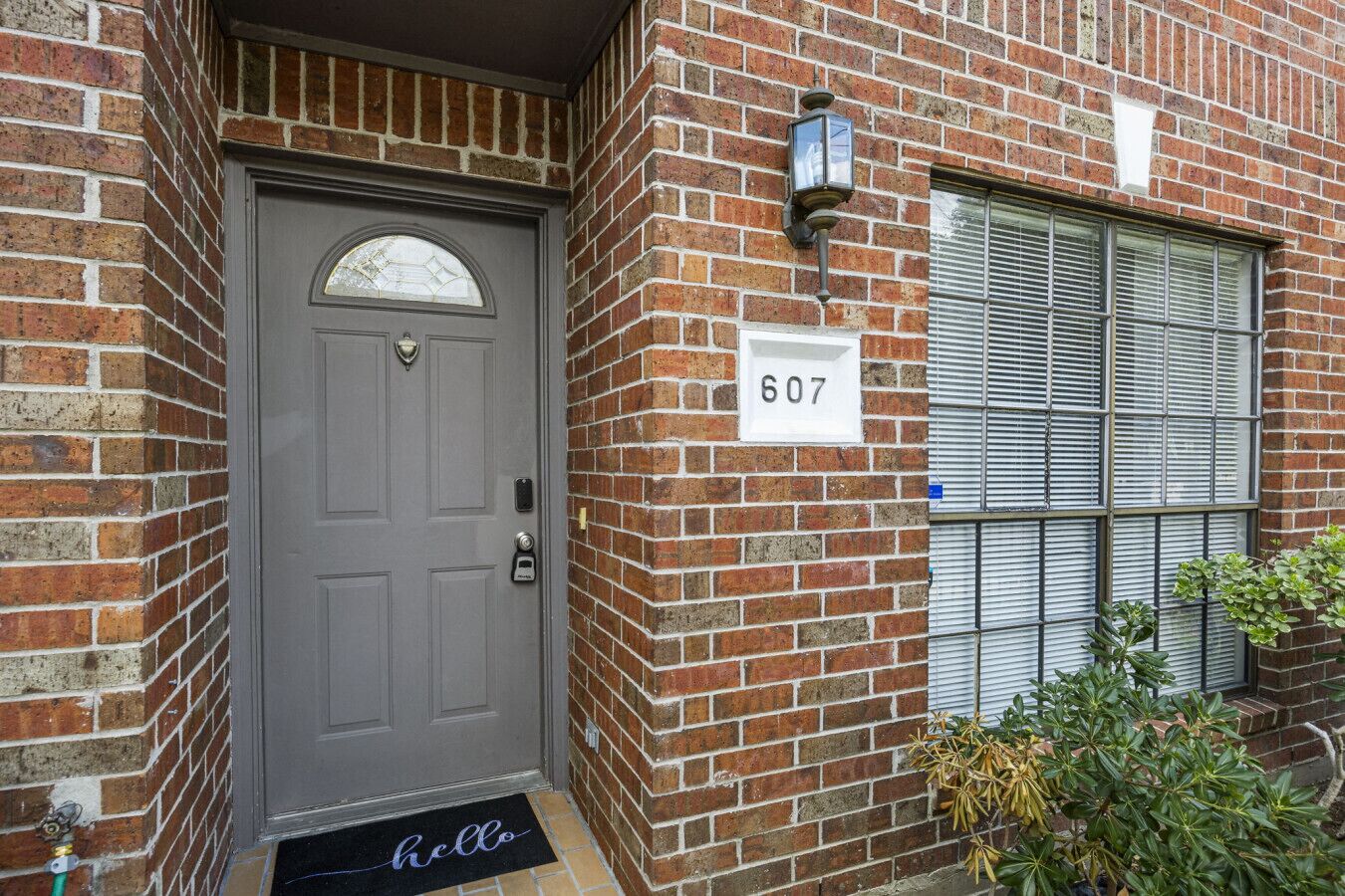 A brick building with a gray door, a number 607 sign, and a window with blinds.