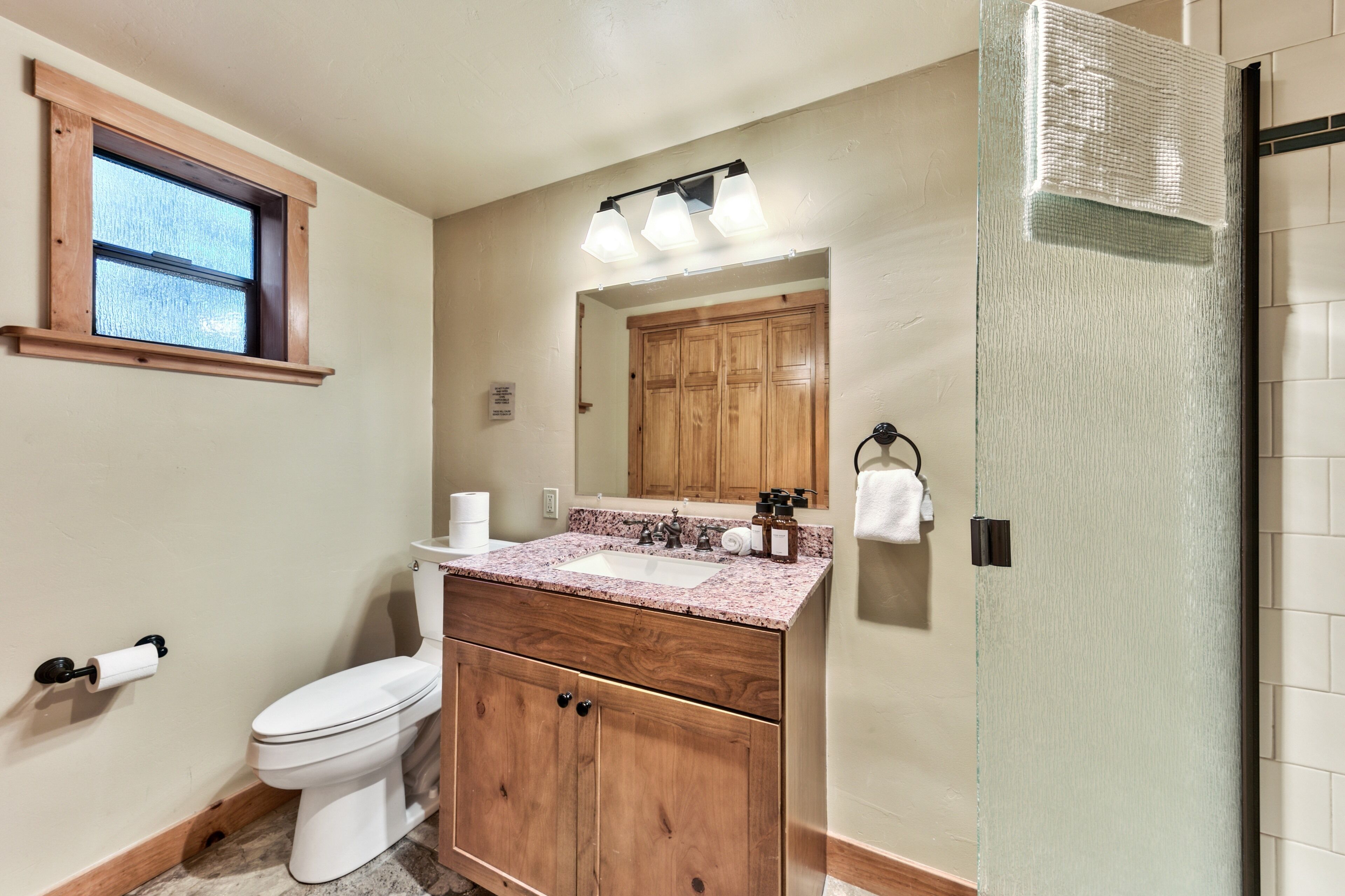 A bathroom with a wooden vanity, a toilet, a sink with a mirror, and a shower area.