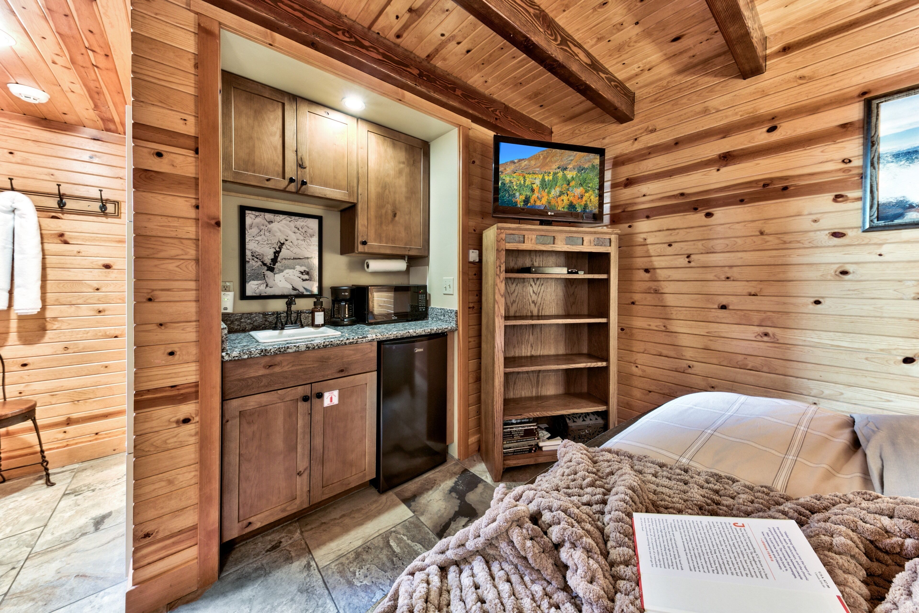A cozy cabin-style room with wooden walls, a kitchenette, a bed with a blanket, and a television.