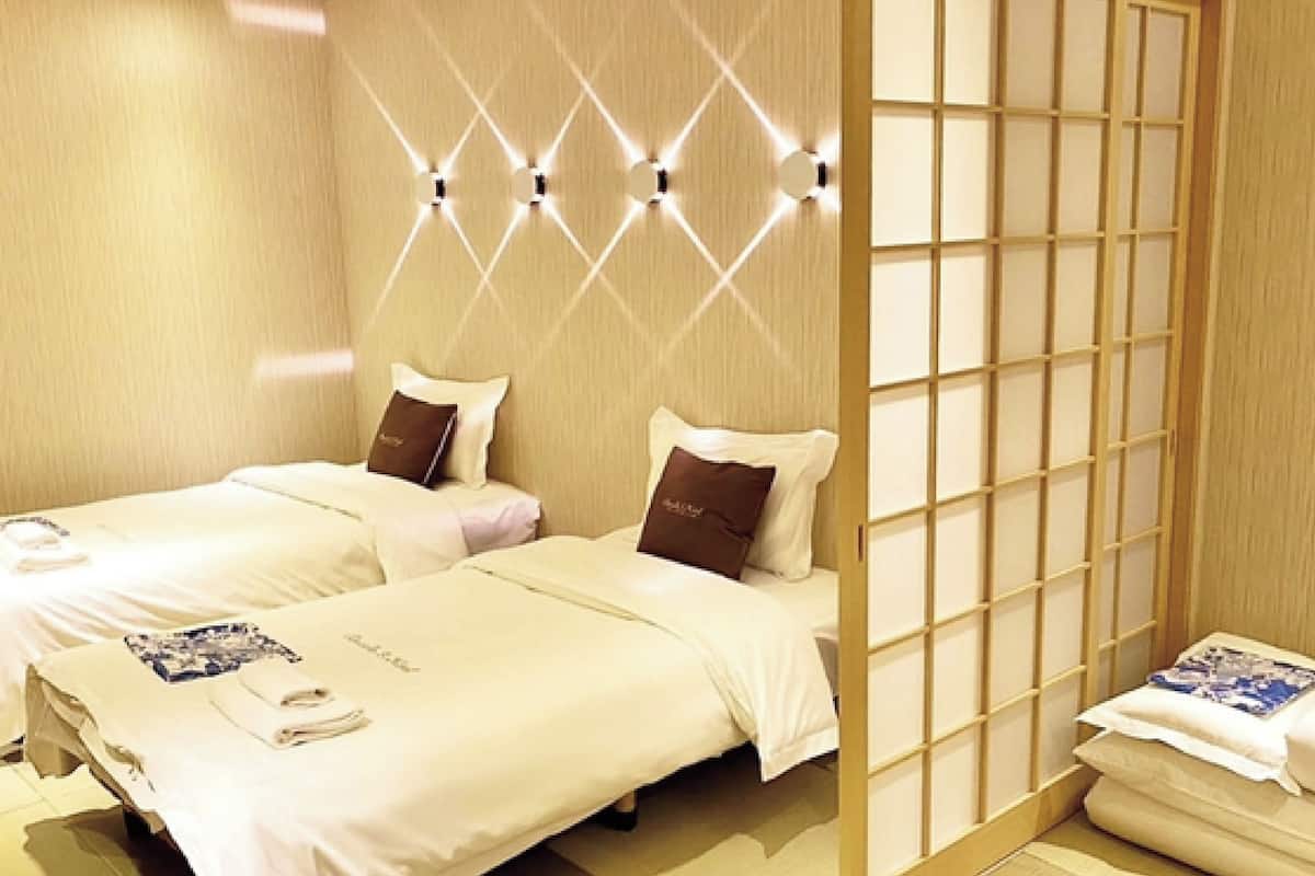 A hotel room with two beds, a wooden partition, and wall-mounted lighting.