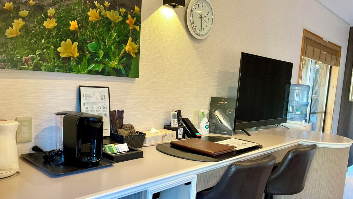 A hotel reception area with a coffee machine, a clock, a television, and a water dispenser.