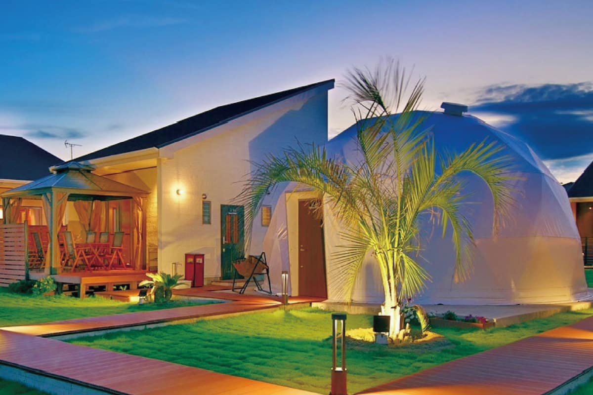 A modern house with a dome structure, a covered outdoor seating area, and a well-maintained lawn.